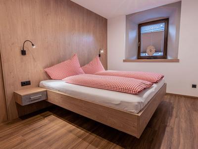 Camera moderna con pavimento in legno, letto matrimoniale, lampade a parete e finestra piccola.