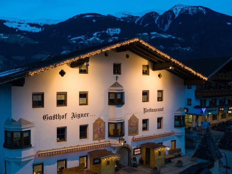 Traditionelles Hotelgebäude mit beleuchteten Fenstern vor dunklem Bergpanorama bei Abenddämmerung.