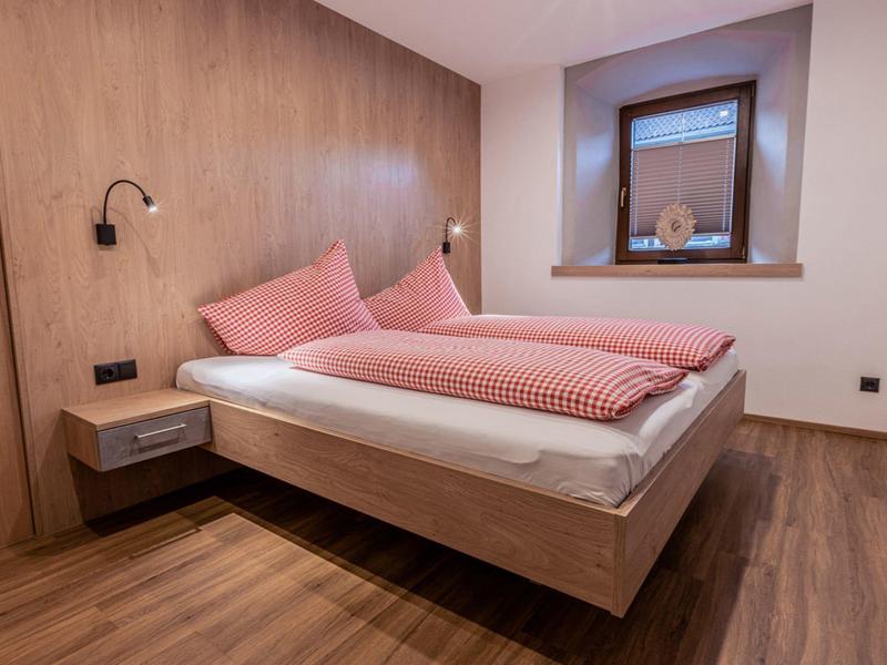 Schlafzimmer mit Holzlaminatboden, Doppelbett mit rosa Bettwäsche und Holzwand mit Leselampen.