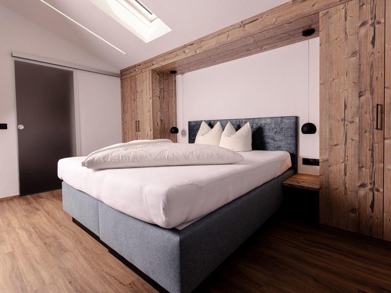 Modernes Schlafzimmer mit großem Bett, Holzakzenten an Wand und Schrank, helles Holzfußboden.