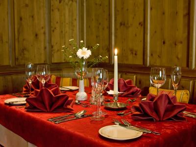 Feestelijk gedekte tafel met rood tafelkleed, kaars en gevouwen servetten in een houten ruimte.