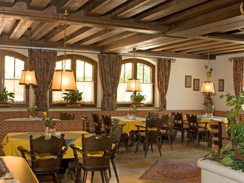 Gemütlicher Gastraum mit Holzbalkendecke, gelben Tischdecken und braunen Holzmöbeln.