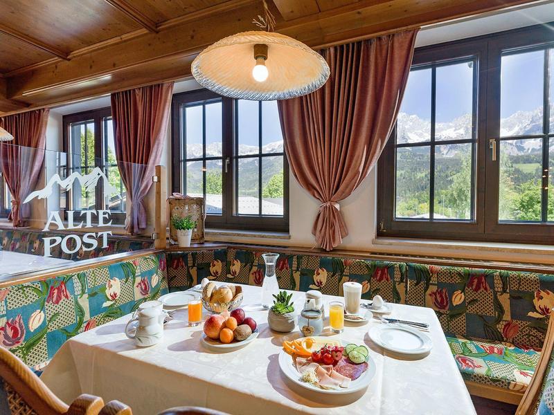 Gemütlicher Frühstückstisch mit buntem Polstersofa, Blick auf Berge und Holzdecke.