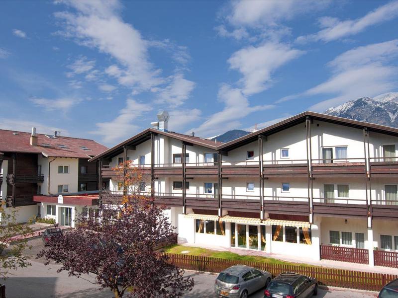 Dreistöckiges Hotelgebäude in Alpenkulisse mit blauem Himmel und leicht bewölktem Himmel.