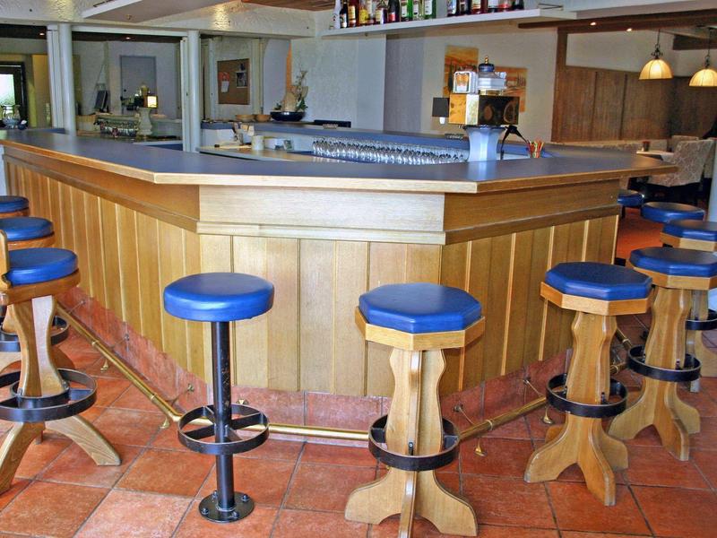 Holzbar mit blauen Sitzkissen auf Hockern, rotbrauner Fliesenboden und helles Raumlicht.