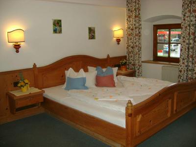 Gemütliches Schlafzimmer mit Holzmöbeln, großem Bett, Nachttisch und Fenster mit Blumenvorhang.