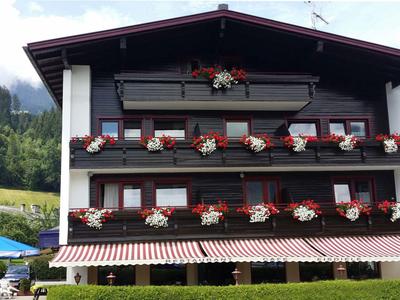 Dreistöckiges Haus mit Holzverkleidung und Balkonen voller roter und weißer Blumen.
