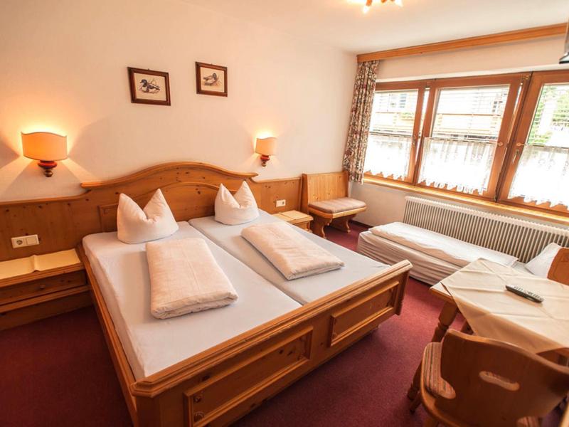 Gemütliches Schlafzimmer mit Doppelbett, Einzelbett, Holzmöbeln und großen Fenstern mit Vorhängen.