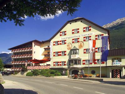 Großes Hotelgebäude mit rot-weißen Fensterläden, davor zwei Fahnen und Berglandschaft im Hintergrund.