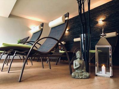 Moderne Entspannungsliegen in dunklem Metall mit grünen Kissen vor einer dunklen Steinwand und Dekoration.