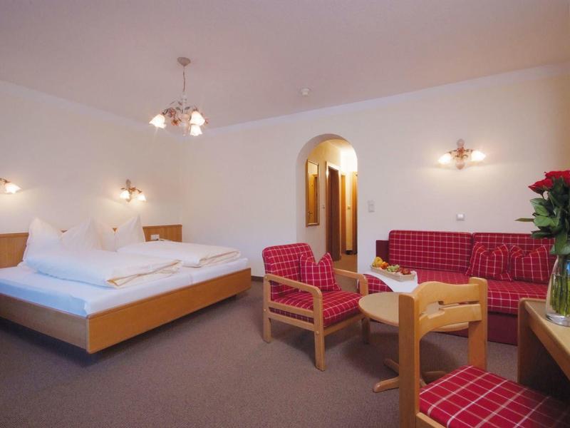 Helles Hotelzimmer mit großem Bett, rot karierten Sesseln, Sofa und einem Holztisch.