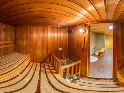 Holzsauna mit geschwungenen Bänken, warmem Licht und Blick in angrenzenden Ruheraum.