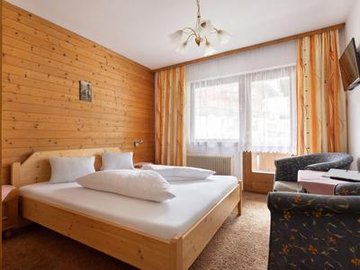 Przytulny pokój hotelowy z drewnianymi panelami, łóżkiem podwójnym, balkonem i miejscem do siedzenia.