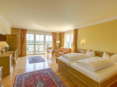 Helles Hotelzimmer mit Doppelbett, Sofa, Teppichen und großem Fenster mit Balkonblick.