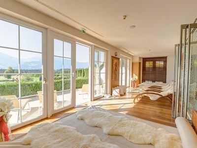 Heller Wellnessraum mit Liegen, großen Fenstern und Blick auf grüne Landschaft und Berge.