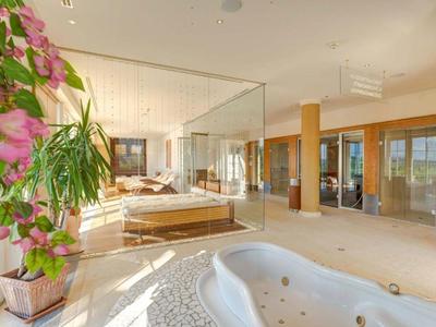 Licht, luxe hotelkamer met groot bubbelbad, bloemen en glazen afscheiding.