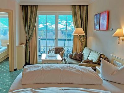 Gemütliches Hotelzimmer mit Doppelbett, Sofa, Sesseln, Balkon und Ausblick auf Berglandschaft.