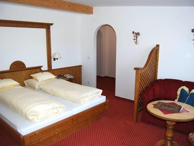 Schlafzimmer mit Doppelbett, rotem Teppich, runder Sitzgruppe und weißer Wand mit Bogen.