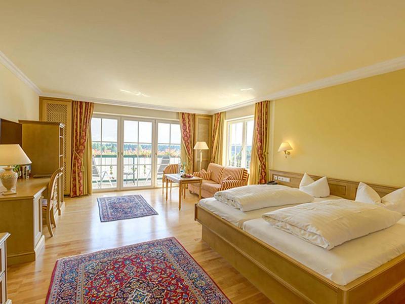 Helles Hotelzimmer mit Doppelbett, Sofa, Teppichen und großem Fenster mit Balkonblick.