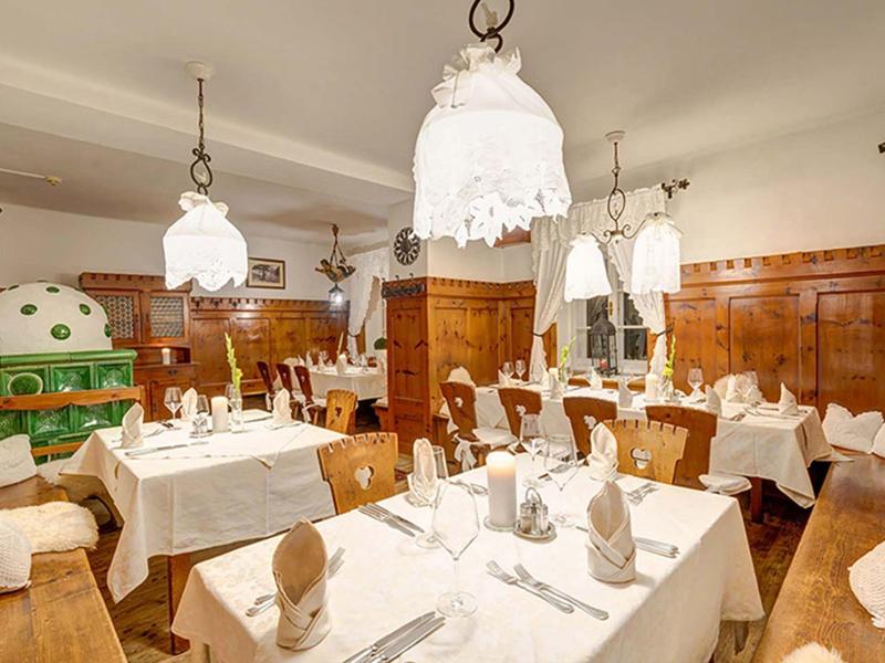 Helles Restaurant mit weißen Tischdecken, Holzwänden, traditionellen Lampen und gedeckten Tischen.