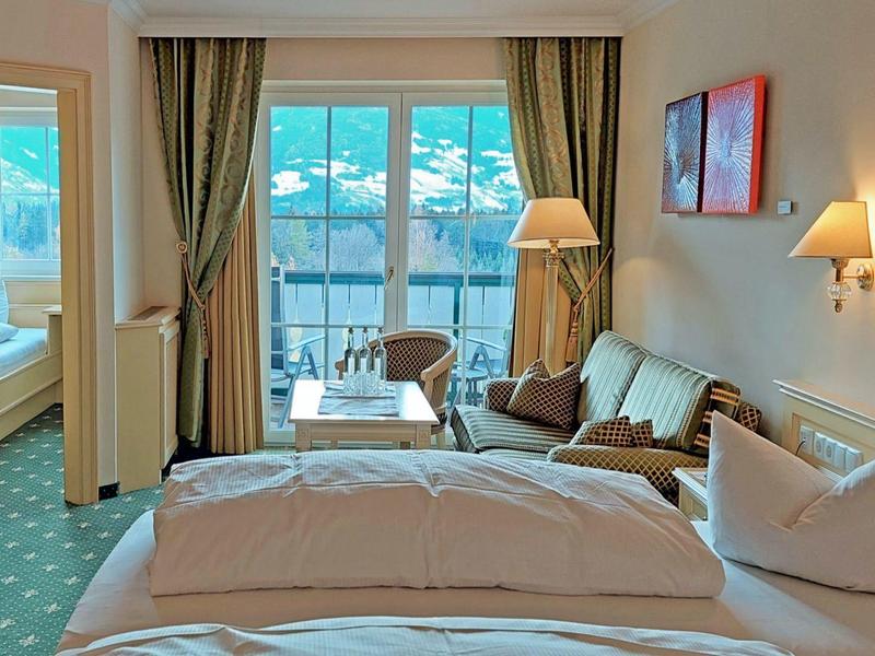Gemütliches Hotelzimmer mit Doppelbett, Sofa, Sesseln, Balkon und Ausblick auf Berglandschaft.