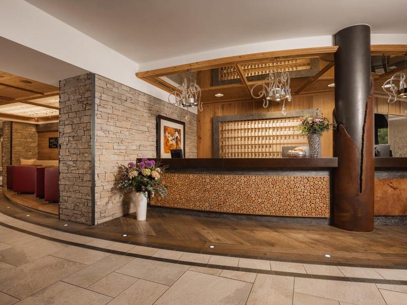 Moderner Hotel-Empfang mit Holztheke, Steinwand und elegant beleuchteter Decke.