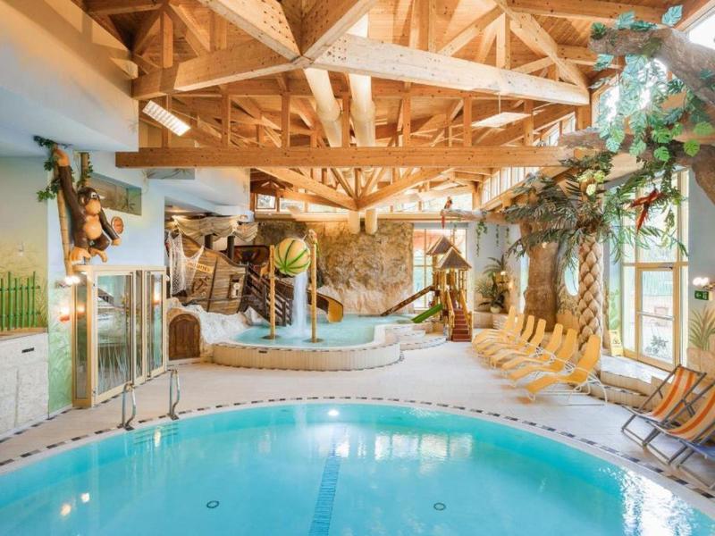 Innenpool mit rundem Becken, Holzbalken-Decke, Liegen und tropischer Pflanzen-Dekoration.