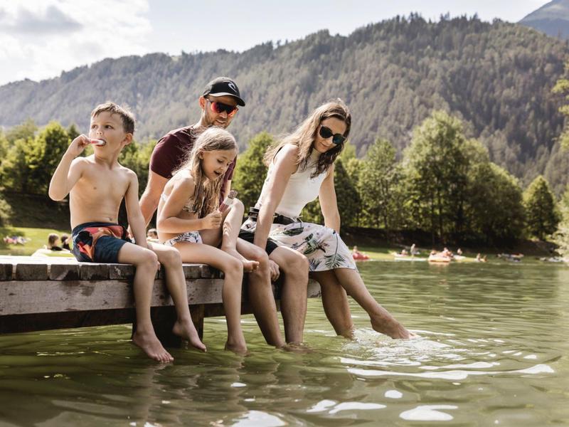 Familie entspannt an einem Steg und taucht ihre Füße ins Bergsee-Wasser.
