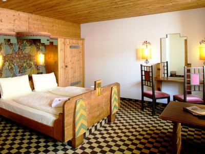 Gemütliches Zimmer mit Holzmöbeln, Doppelbett, Schreibtisch und geschwungenem Teppichboden.