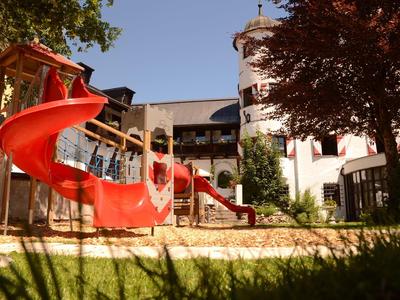 Rote Rutsche auf einem Spielplatz vor einem Hotelgebäude bei sonnigem Wetter.