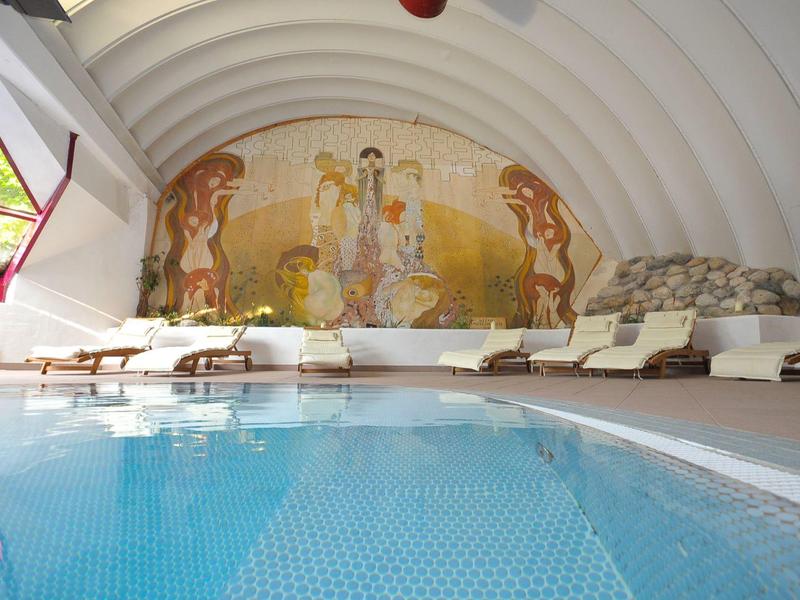 Innenpool mit Liegestühlen und Wandmalerei in einem abgerundeten Raum mit Fenster