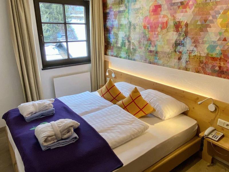 Modernes Hotelzimmer mit Doppelbett, buntem Wandbild und Fenster mit Blick ins Grüne.