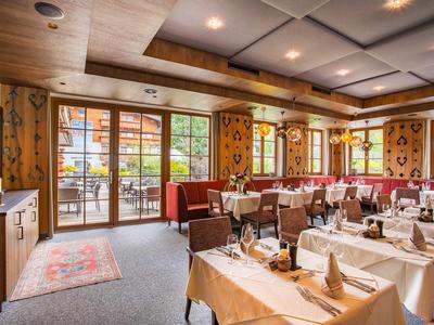 Helles Restaurant mit gedeckten Tischen und Holzdecke, großen Fenstern mit Blick auf Terrasse.