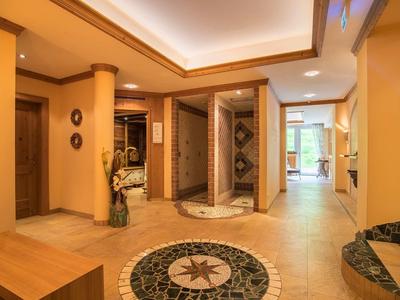 Warmer Hotellobbybereich mit zentralem Mosaik, Holzmöbeln und Zugang zu verschiedenen Zimmern.