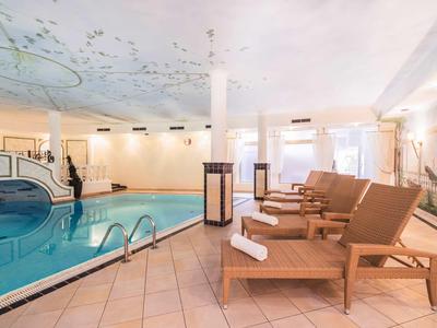 Piscina interna luminosa con sdraio in legno e acqua blu pulita in un hotel.