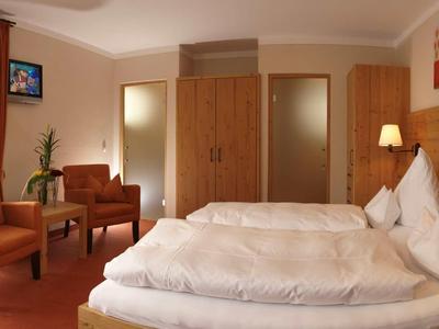 Camera d'hotel accogliente con due letti, poltrone e armadio in legno in tonalità calde