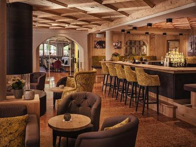 Area bar accogliente in hotel con soffitto in legno, sgabelli e poltrone imbottite in tonalità calde.
