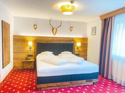 Gemütliches Schlafzimmer mit großem Bett, rotem Teppich und Holzwandverkleidung mit Hirschgehörn.