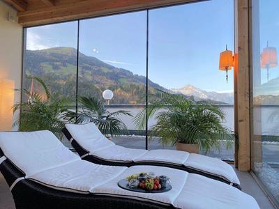 Zwei weiße Liegen mit Kissen auf Terrasse, dahinter Glaswand mit Berg- und Himmelsblick.