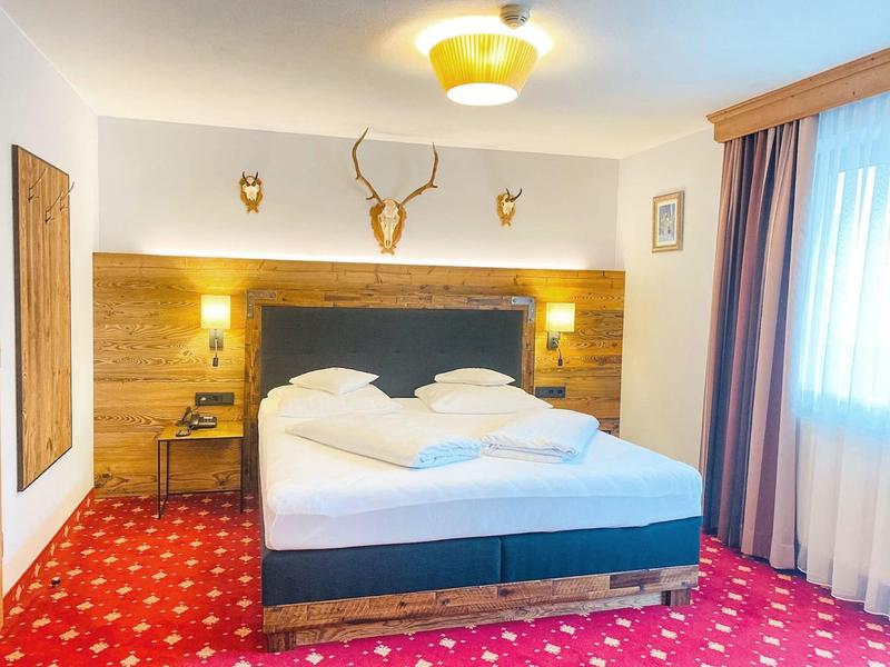 Gemütliches Schlafzimmer mit großem Bett, rotem Teppich und Holzwandverkleidung mit Hirschgehörn.