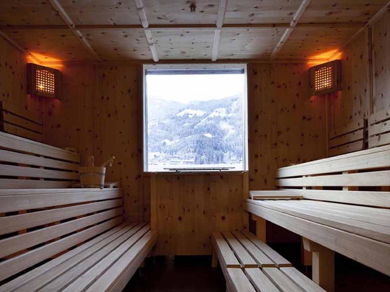 Holzsauna mit Bänken, Fenster mit Bergblick, warme Beleuchtung an den Wänden.