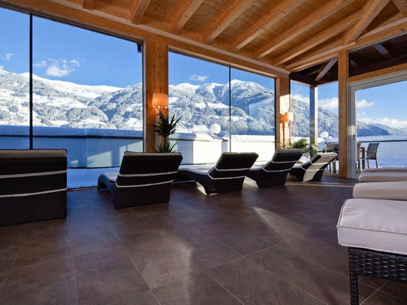 Innenraum mit Holzdecke, großen Panoramafenstern und Liegestühlen mit Blick auf schneebedeckte Berge.