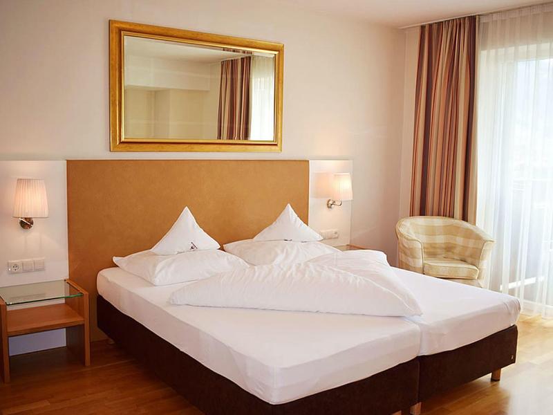 Gemütliches Schlafzimmer mit zwei Einzelbetten, großen Fenster und hellem Sessel am Fenster.