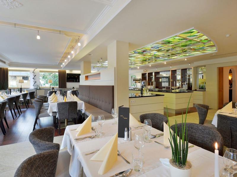 Elegantes Restaurant mit gedeckten Tischen, weißen Tischdecken und modernem Deckenlicht mit Pflanzenmotiv.