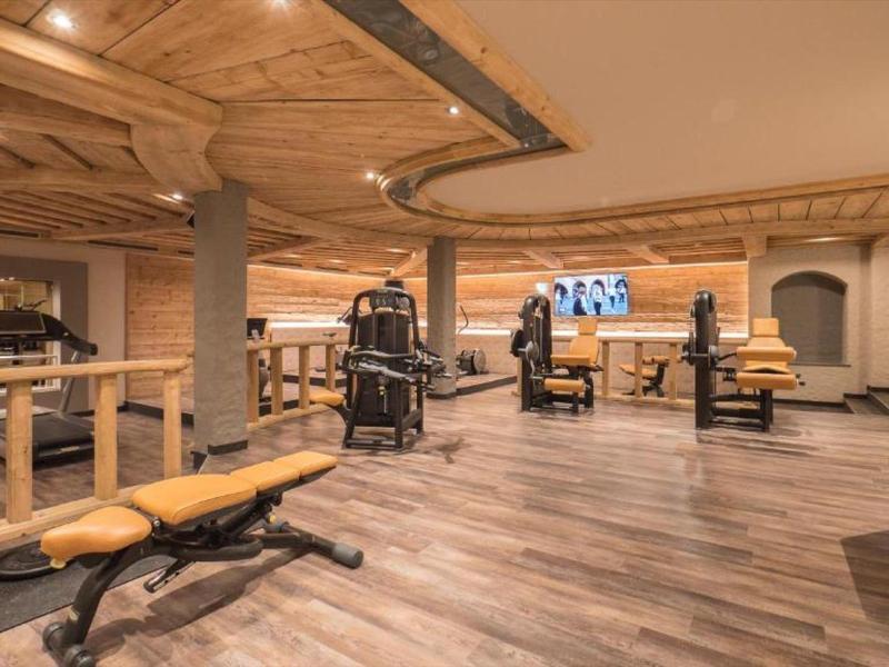 Großer Fitnessraum mit Holzdecke, Kraftgeräten, Hantelbänken und Fernsehern an der Wand.