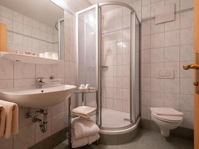 Kleines Badezimmer mit weiß gekachelter Dusche, Waschbecken, WC und Holzregal mit Handtüchern.