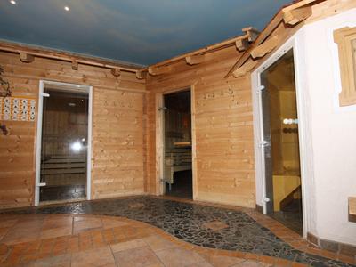 Innenansicht eines Wellnessbereichs mit Holzsaunen, Fliesenboden und einer blauen Decke.