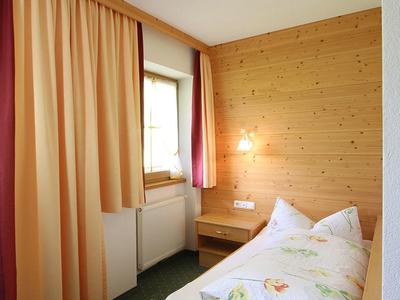 Kleines Schlafzimmer mit Holzverkleidung, grünem Teppich, Einzelbett und beige-roten Vorhängen.