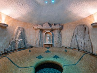 Rundes Zimmer mit steiniger Wand, beleuchtet durch Wandlampen, und einem hufeisenförmigen Becken.