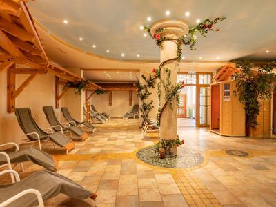 Innenraum eines Wellnessbereichs mit Liegestühlen, Säule mit Pflanzen und warmem Licht.